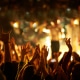 Audience with hands raised at a music festival and lights streaming down from above the stage. Selective focus.